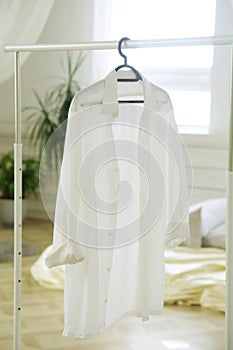 A white women\'s shirt hangs on a hanger in the room