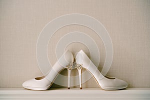 White women`s shoes with high pointed heels, with a pattern of flowers, on a gray background.