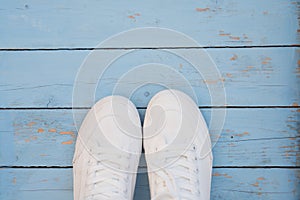 White women`s sneakers on a blue boardwalk background. Clean white sneakers in the center of the frame on the blue wooden floor.