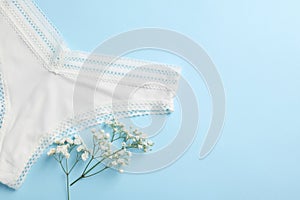 White women's underwear and flowers on light blue background, flat lay. Space for text