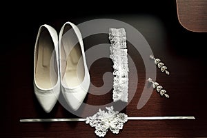 White women`s wedding shoes, garter, earrings on a dark wooden background photo