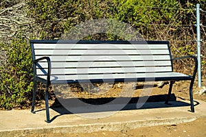 White wood bench with black gaurd rails and fram on side of park or outdoor area or suburban neighborhood in light photo