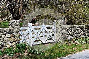 A white wood cross-braced gate is set in a stone wall alongside a road