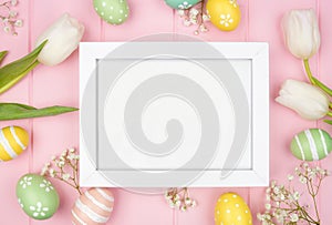 White wood frame with Easter eggs and spring tulip flowers against a pink wood background