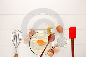 White Wooden Baking Background with Basic Baking Utensil and Ingredients. Egg, Ballon Whisk, Flour, Oil, and Spatula on the Right