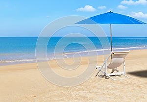 White wooden beach chair and blue parasol on tropical beach