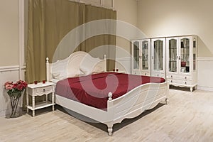 White wooden bed with dark red blanket and white pillows.