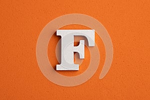 White wooden capital letter F on orange foamy background