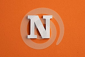 White wooden capital letter N on orange foamy background