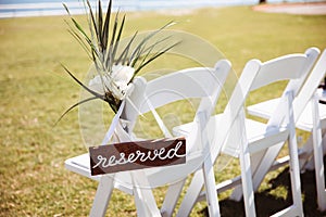 White wooden chair with rustic Reserved sign on green lawn . Outdoor wedding ceremony