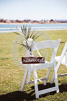 White wooden chair with rustic Reserved sign on green lawn . Outdoor wedding ceremony