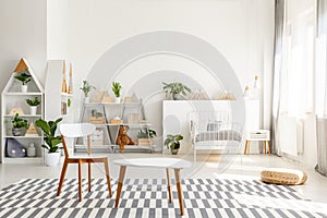 White wooden chair and table set, green plants in a spacious, sunlit teenager bedroom interior with scandinavian decor