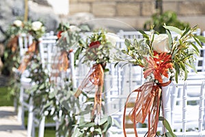 White wooden chairs decorated with flowers and lush greenery as part of a wedding ceremonial setup