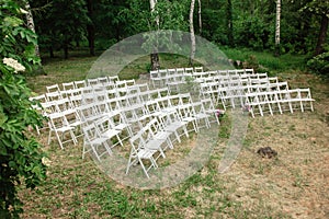 White wooden chairs placed in rows on the lawn. Place for wedding ceremony or other events in botanic garden. Seats for visitors