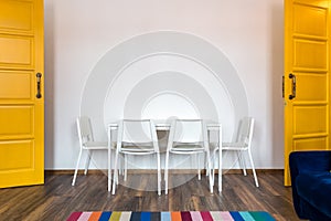 White wooden chairs with a table against the background of a white wall in the interior with yellow doors