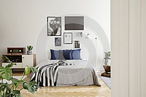 White wooden commode next to bed with dark blue pillows, grey duvet and striped black and white blanket in bedroom