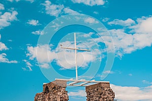 A white wooden cross against a blue sky with clouds, a seagull sits on the edge