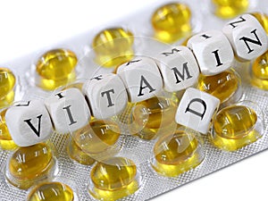 white wooden cubes with black letters form the text Vitamin D on yellow pill blister