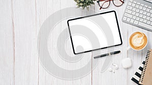 White wooden desk workplace with blank screen tablet, keyboard, pen, eyeglass, notebook and cup of coffee,