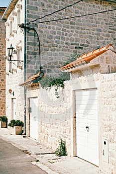 White wooden doors in the old stone wall of the house with red tile visors