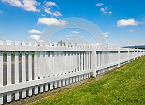 White wooden fence on the blue sky background. Green lawn and wooden white fence on sunny summer day