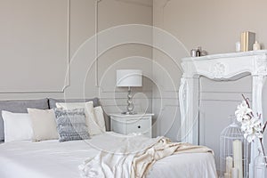 White wooden fireplace portal in beautiful bedroom interior with white sheets on king size bed
