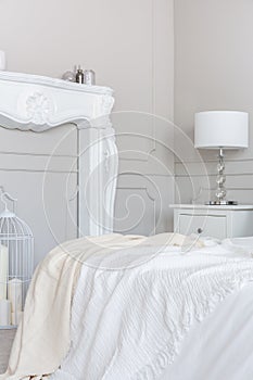 White wooden fireplace portal in beautiful bedroom interior with white sheets on king size bed