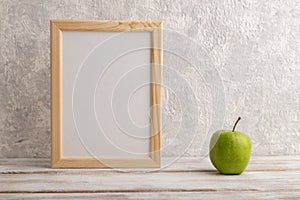 White wooden frame mockup with green apple on gray concrete background. Blank, vertical orientation, copy space