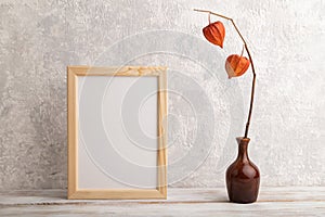 White wooden frame mockup with physalis in ceramic vase on gray concrete background. Blank, vertical orientation, copy space