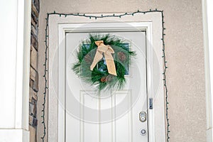 White wooden front door with Christmas wreath and string lights on the doorframe