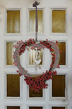 White wooden front door decorated in autumn, with red leaves, berries and a wreath