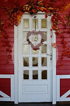 White wooden front door decorated in autumn, with red leaves, berries and a wreath