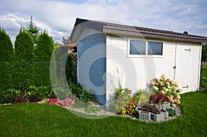 White wooden garden shed or hut with flowers and plants