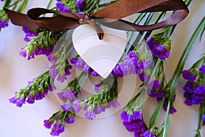White wooden heart with brown silk bow on statice purple potpourri flowers on white background. Love concept. St. Valentine`s