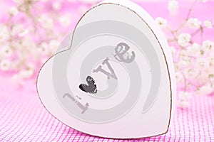 White wooden heart closeup with word Love, on pink mesh fabric and white flowers