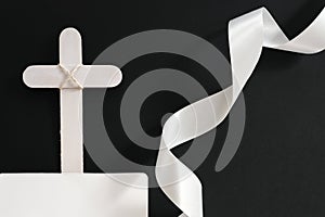 White wooden memorial cross with white ribbon in black background.