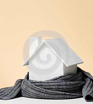 A white wooden miniature house wrapped in a gray knitted scarf. Building insulation concept, loans for repairs