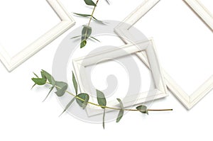 White wooden photo frame and green eucalyptus leaves on white background. Flat lay top view copy space. Stylish minimal