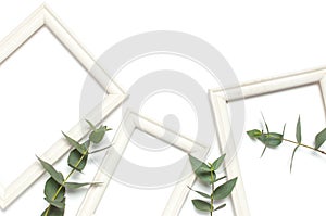 White wooden photo frame and green eucalyptus leaves on white background. Flat lay top view copy space. Stylish minimal