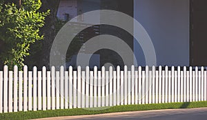 White wooden picket fence on artificial turf with sunlight and shadow on surface in front yard area at home