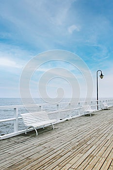 White wooden pier, blue sky, sea. White benches on the pier.