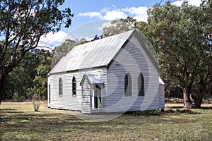 White wooden rural country church with arched windows set against bushland background