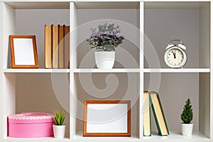 White wooden shelves with books and flowers in a pot photo frames. Home interior, decor elements