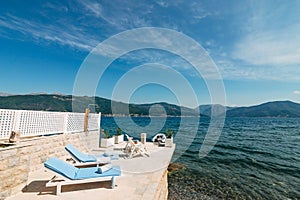 White wooden sunbeds on the pier, by the sea. In the Bay of Kotor, in Montenegro. Azure blue water and pebble bottom