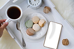 White wooden tray with black tea, coffee, plate with macaroon cakes, alarm clock, blank screen phone, concept of technology, time