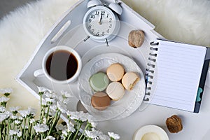 White wooden tray with black tea, coffee, plate with macaroon cakes, flowers, candles, notebook with blank sheets for text,