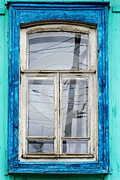 White wooden window with blue platbands in the wall of an old green wooden house