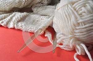 White wool knitting needles and handmade knits on bright orange background