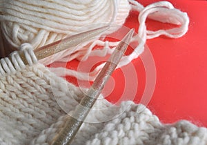 White wool knitting needles and handmade knits on bright orange background