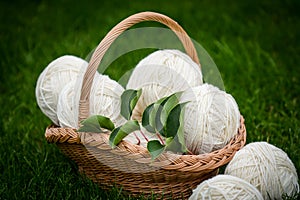 White woolen yarn in basket on green background